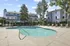Inviting apartment community featuring a pristine outdoor pool surrounded by modern lounge chairs, set against stylish blue and white buildings amid lush greenery.