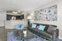 Bright and modern living room with a stylish gray sofa, vibrant abstract art, and open kitchen view featuring sleek dark cabinetry and stainless steel appliances.