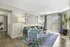 Chic, sunlit living room with modern decor, featuring a cozy gray sofa, stylish blue armchair, vibrant abstract art, and large windows inviting natural light.