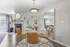 Modern living area featuring elegant glass dining table with leather chairs, stylish decor, and a cozy fireplace, bathed in natural light.
