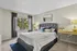 Inviting bedroom with plush gray bed, elegant decor, large window overlooking greenery, and modern workspace.