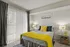 Bright and inviting bedroom with modern decor, featuring a cozy bed adorned with vibrant yellow accents and a large window with elegant vertical blinds.