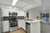 Modern kitchen with sleek stainless steel appliances, spacious countertops, and elegant cabinetry, opening into a bright living area with sliding doors to a balcony.