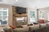 Elegant living room featuring a stone fireplace with a mounted TV, plush seating, and large windows overlooking a serene outdoor pool area.