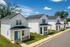 Charming row of modern white houses, each with a welcoming porch and vibrant blue door, set against a lush green backdrop and clear blue skies.