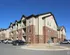 Modern multi-story apartment complex with charming brick and siding exterior, ample parking, and clear blue skies, perfect for comfortable living.