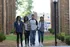 Four friends enjoying a sunny day walk through a modern apartment complex with beautiful landscaping and brick architecture.