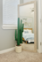 Chic bedroom corner with a tall cactus in a stylish planter, a large mirror reflecting cozy bedding and decorative accents, enhancing natural light and elegant decor.