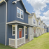 Charming townhouses with classic blue and white exteriors, featuring quaint porches and lush green lawns.