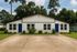Charming duplex with crisp white facade and bold blue doors, surrounded by lush greenery in a serene suburban setting.