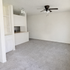 Inviting living area with plush carpeting, modern ceiling fan, and ample natural light, adjacent to an open kitchen space with sleek cabinetry and cozy breakfast bar.
