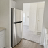 Bright kitchen entryway featuring modern stainless steel refrigerator, white cabinetry, and a cozy view into the carpeted living area.