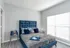 Chic bedroom with plush blue bed, stylish side tables, and abundant natural light through large window.