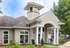 Charming apartment entrance with elegant columns, stone facade, and lush landscaping under a bright blue sky.