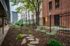 Charming courtyard featuring green metal chairs, lush landscaping, and a modern urban backdrop.