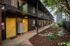 Modern apartment exterior with vibrant yellow doors, lush landscaping, and cozy seating area, offering a welcoming and stylish entrance.