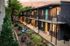 Charming two-story apartment block with vibrant doors and elegant outdoor seating, surrounded by lush greenery at sunset.
