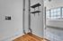 Bright apartment corner showcasing sleek wood flooring, modern shelving, and a glimpse of the large window with urban views.