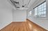 Bright apartment room showcasing polished hardwood floors, large windows with serene views, and industrial-style ceiling fan with exposed ductwork.