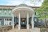 Inviting apartment entrance with elegant columns and charming stone walkway, surrounded by lush greenery and classic architectural details.