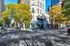 Charming urban street scene with vibrant trees, classic architecture, and bustling city life.