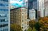 Charming urban apartment building nestled among vibrant skyscrapers, surrounded by lush autumn trees in a bustling cityscape.