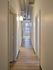 Chic apartment hallway with modern industrial ductwork and sleek wood flooring, leading to a bright window.