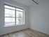 Bright and airy apartment room with expansive window and modern light wood flooring, offering a charming urban view.