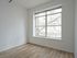Bright and airy apartment room with a large window and sleek wood flooring, perfect for modern urban living.