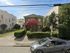 Charming two-story house with a lush front garden, vibrant red tree, and welcoming pavement in a peaceful neighborhood.