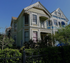 Charming Victorian-style home with intricate architectural details, vibrant colors, and lush greenery.