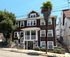 Charming multi-story brown shingle house with white trim, nestled among lush greenery in a beautiful suburban neighborhood.