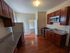Charming kitchen with elegant cherry wood cabinets, modern appliances, and sleek granite countertops, leading into a bright adjoining room with warm wooden floors.