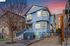 Charming blue multi-story house with bay windows and a welcoming front staircase, set against a vibrant sunset sky.