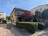 Charming two-story home with classic architecture, vibrant greenery, and a welcoming entrance bathed in sunlight on a serene street.