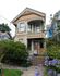 Charming Victorian-style house with elegant trims, vibrant garden, and welcoming porch surrounded by lush greenery and blooming flowers.