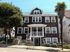 Charming multi-story brown shingle building with welcoming porch, set in a vibrant neighborhood with lush trees and a classic palm, exuding character and curb appeal.