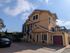 Charming multi-story yellow home with a spacious driveway and inviting balcony, bathed in sunlight under a clear blue sky.
