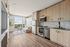 Modern apartment interior showcasing a stylish kitchen with stainless steel appliances and sleek wooden cabinetry, combined with a cozy living area featuring large windows offering scenic views.