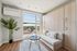 Bright, modern apartment living space featuring sleek wood cabinetry, a cozy sofa, elegant potted plant, and expansive window with cityscape views.