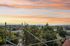 Stunning sunset view from a high-rise apartment overlooking a lush green landscape and a distant city skyline.