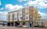 Modern urban apartment complex with sleek architecture, large windows, and street-level businesses under a vibrant blue sky.