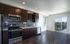 Modern apartment kitchen with sleek dark cabinets, stainless steel appliances, and bright natural light pouring through glass doors leading to a balcony with scenic views.