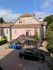 Charming pink house with a spacious driveway and upper deck, set against a backdrop of lush greenery and a clear blue sky.