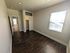 Bright and inviting bedroom with elegant hardwood floors and natural light streaming through a large window, leading into a stylish tile-floored hallway.