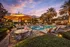 Inviting evening poolside at luxury apartments, featuring sun loungers, vibrant umbrellas, and lush palm trees under a colorful sky.