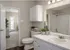 Elegant bathroom with white cabinetry, a large mirror, and stylish decor, leading to a bright room with plush carpeting and a glass door.