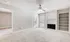 Inviting living room with cozy carpet, a bright white brick fireplace, and ample natural light from large windows. Ideal for relaxing and entertaining.