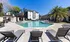 Luxurious outdoor pool area with stylish lounge chairs, surrounded by modern apartment buildings and lush palm trees under a clear blue sky.