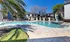 Inviting apartment pool area with sun loungers, a sparkling fountain, and lush landscaping under a sunny blue sky.